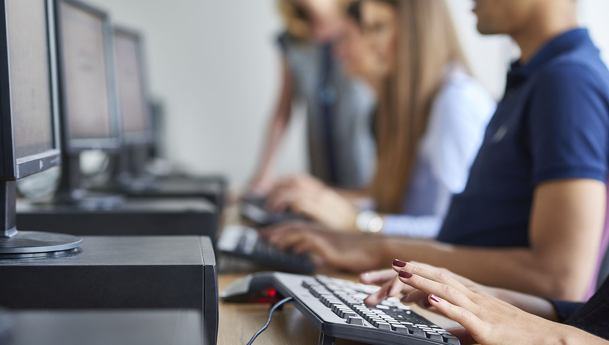 Here are a row of students using computers.They are all in the classroom working hard.The teacher is checking on her students.