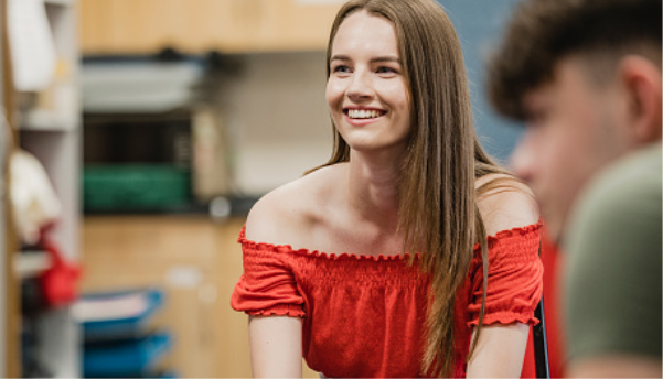 A teenage girl in a red top smiling in class.