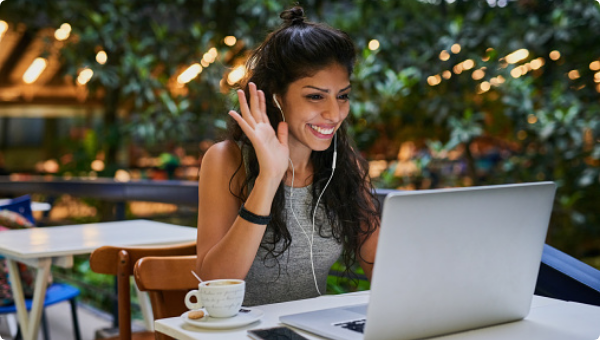 A woman working in a cafe waving at her laptop