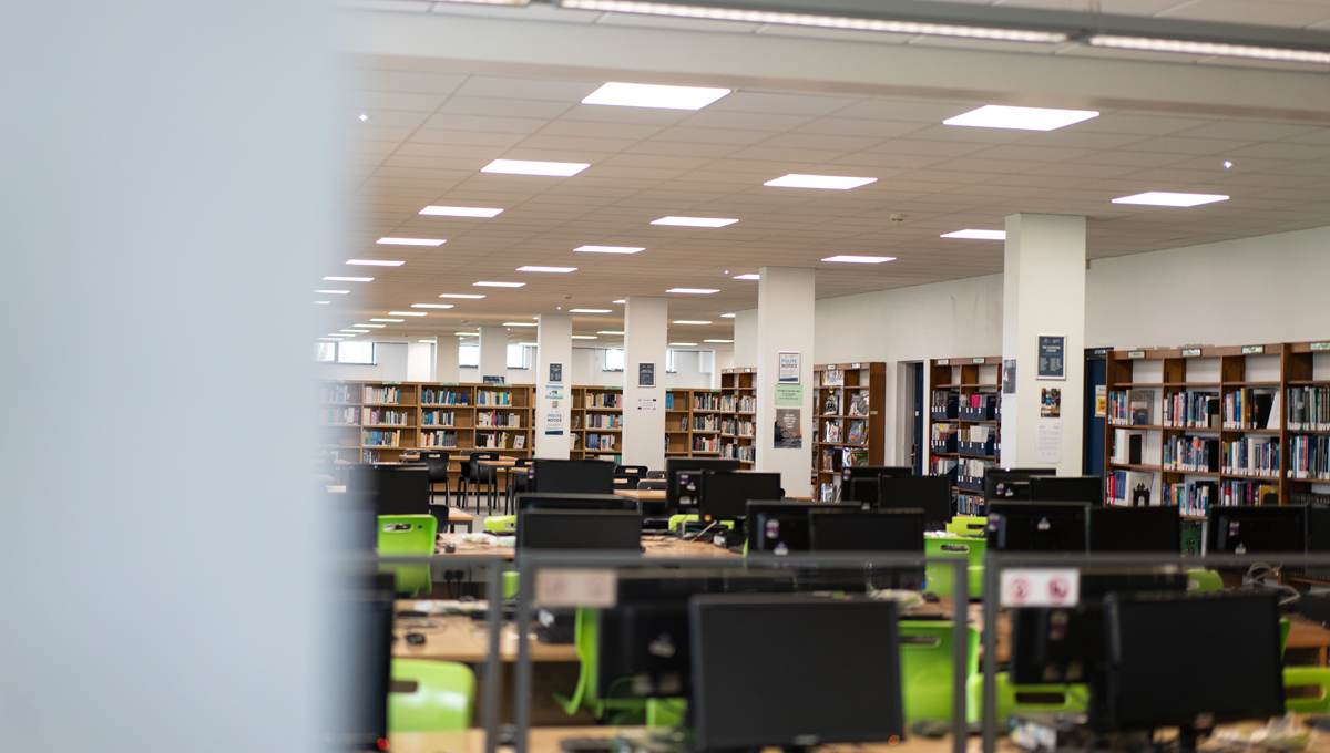 A library with books stacked along the walls and decks with computers in the centre