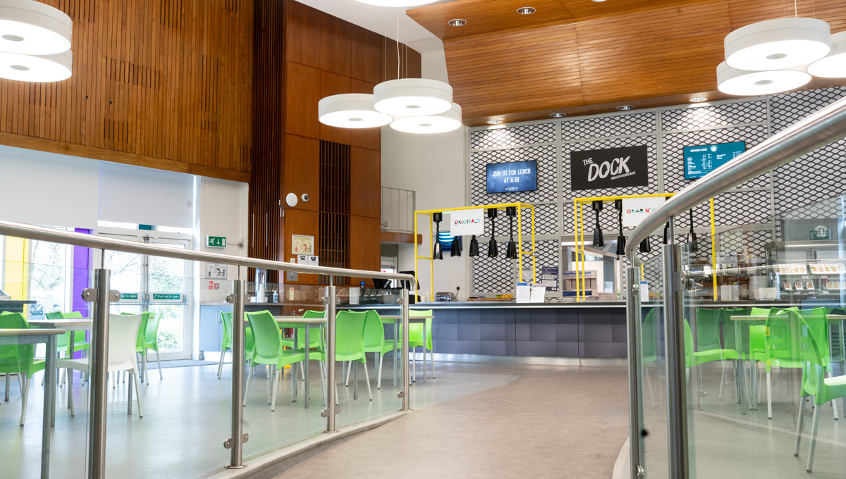 A cafe with green chairs and a glass railing.