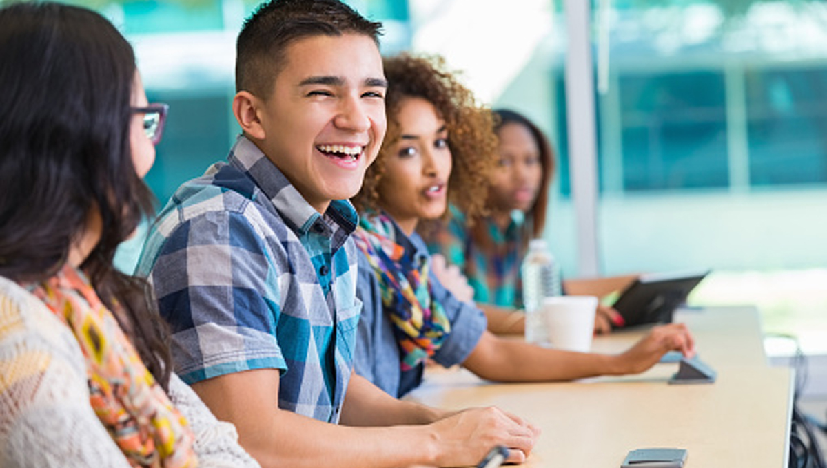 High school or college student laughing with classmates at desk