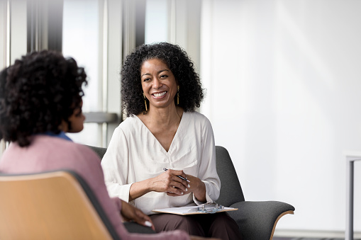 Mature adult female therapist smiles broadly as her unrecognizable mid adult female client shares her story.