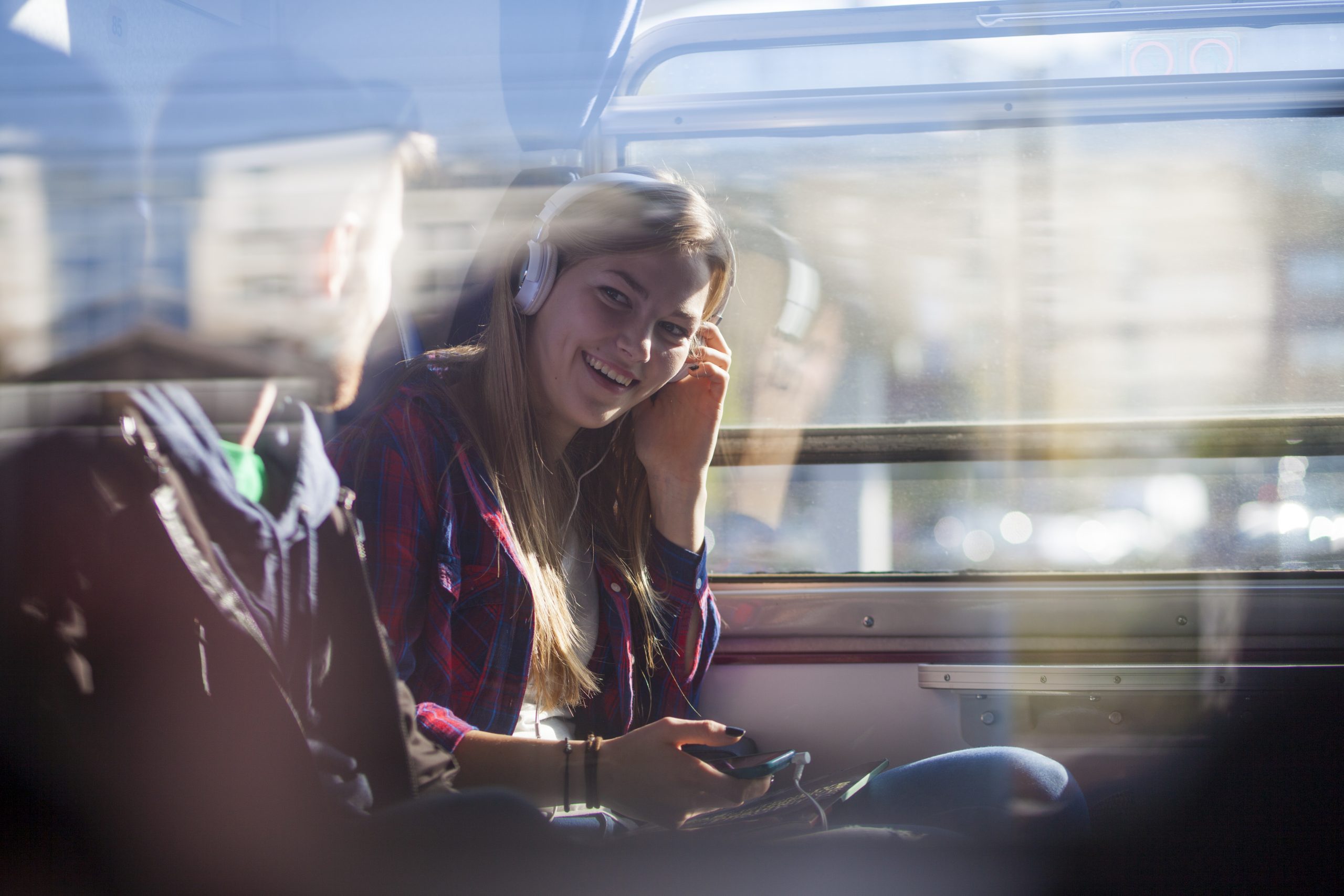 Through the train window look at a couple talking. Woman with headphones on her head. Smiling to the man beside her.