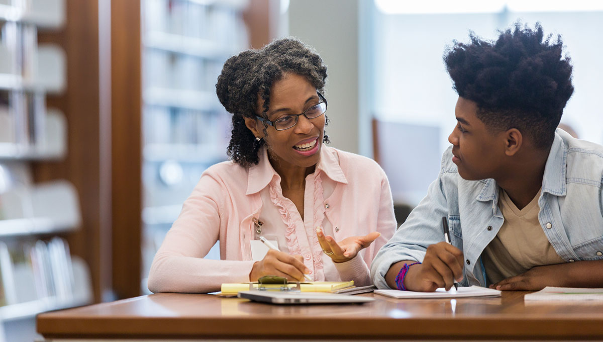 Volunteer mentors teen boy in school library