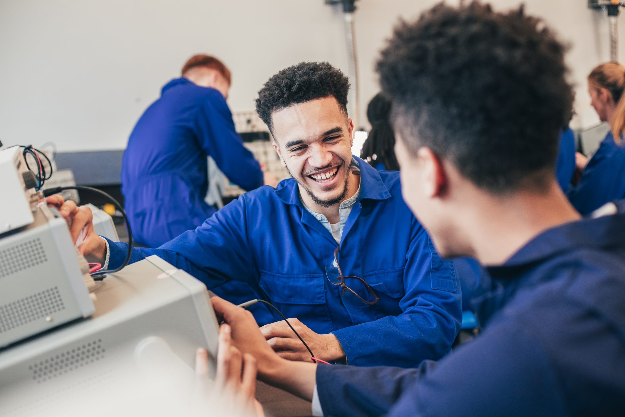 Two mixed race engineering students work on a group project together in a workshop. They are both wearing blue coveralls.