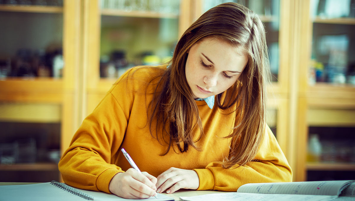 Young female college student in chemistry class, writing notes. Focused student in classroom. Authentic Education concept.