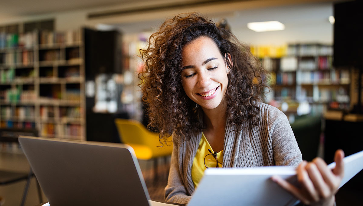 Young afro american woman sitting at table with books and laptop for finding information