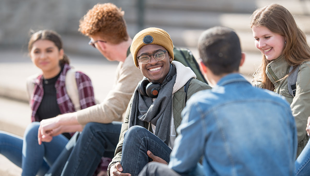 A multi ethnic group of university students are hanging out outdoors on campus.