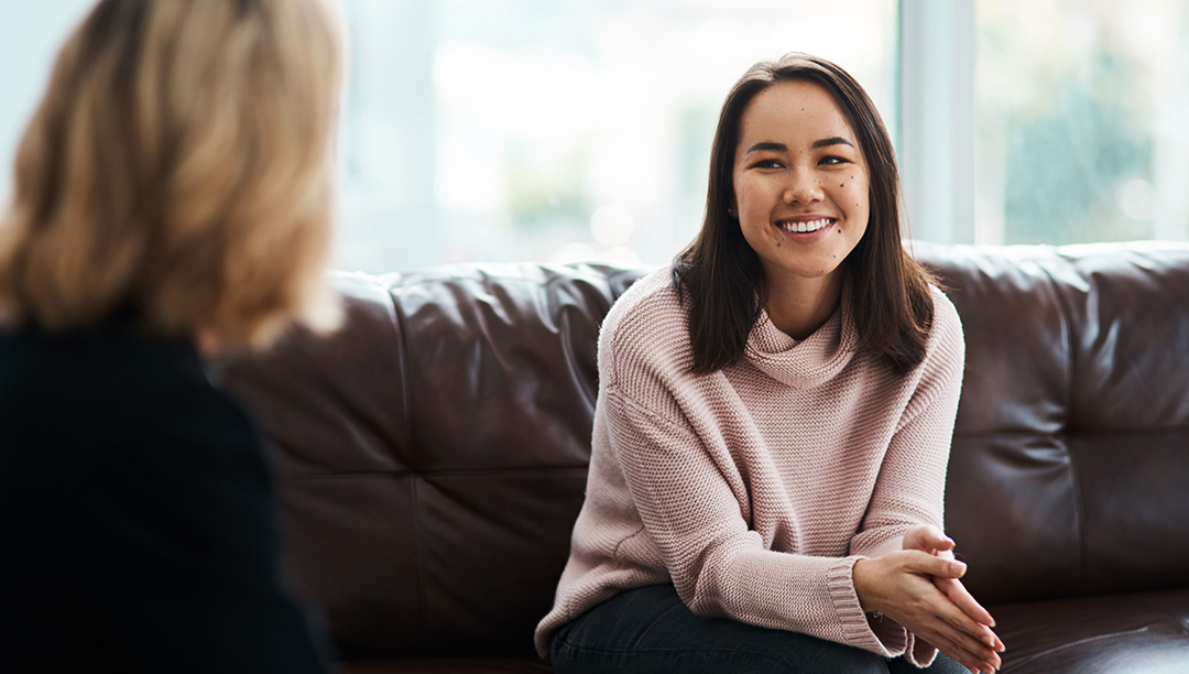 A woman sat on a leather sofa smiling talking to a lady