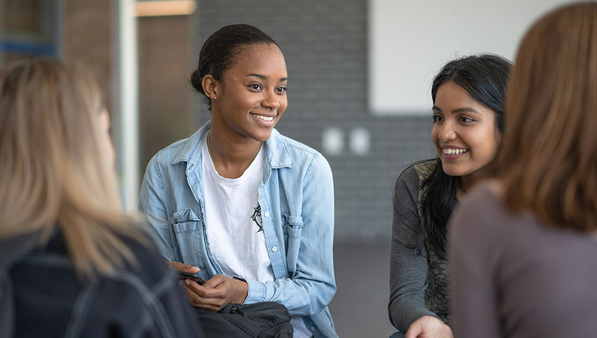 A group of multi ethnic females talking and smiling with each other as they are all part of a group therapy session. They have each other as support.