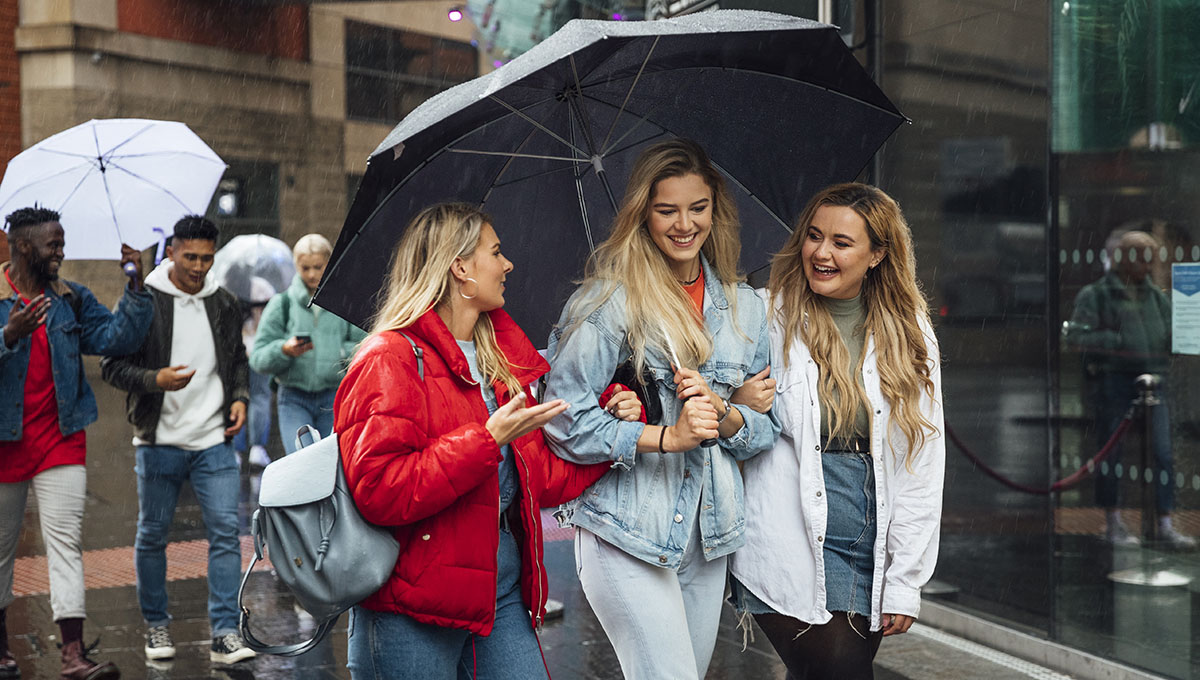 A group of friends meeting up and looking to find somewhere to have food on a rainy day in Newcastle upon Tyne city centre the woman in front are sharing an umbrella.
